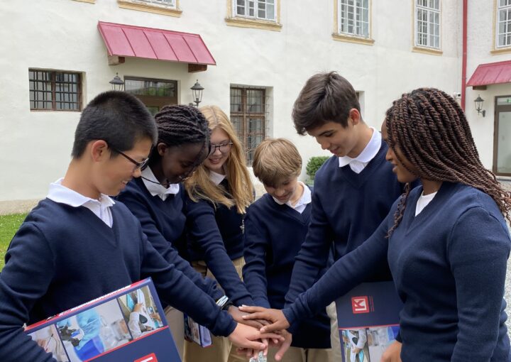 Diverse group of students in school uniforms joining hands outside a school building