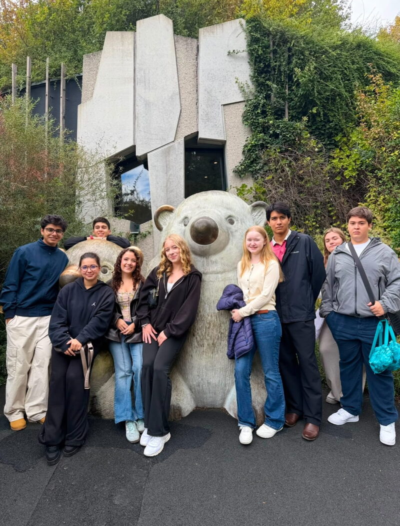 Students gather around large koala sculptures outside an ivy-covered zoo building.