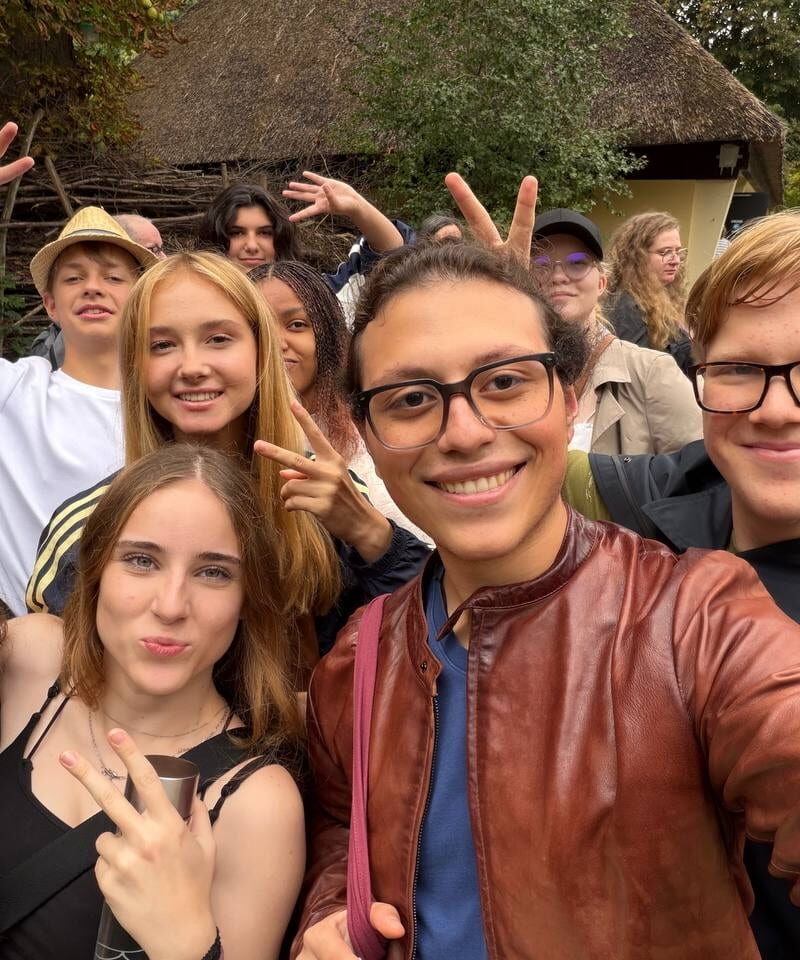 A group poses for a close-up selfie on a zoo path, smiling and making peace signs.