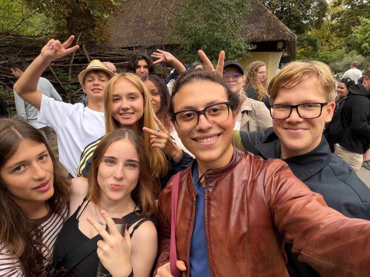 A group poses for a close-up selfie on a zoo path, smiling and making peace signs.