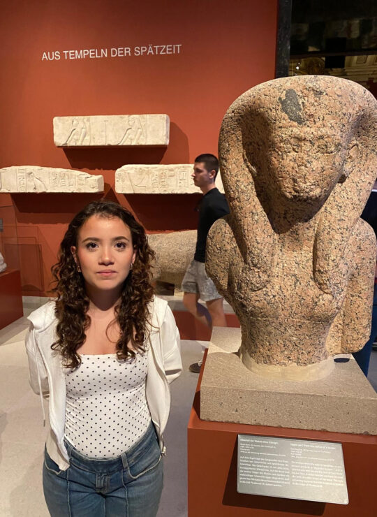 One of our students crouches beside an Egyptian sphinx displayed in a glass case.