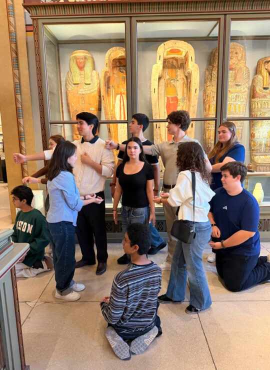 Our students strike coordinated poses in front of a glass display of Egyptian coffins.