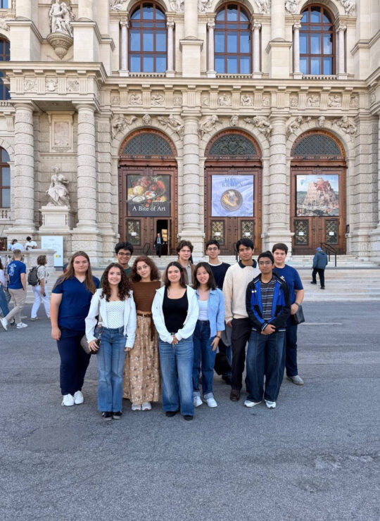 Our Schloss Krumbach International School students pose outside an ornate museum entrance beneath exhibition posters.