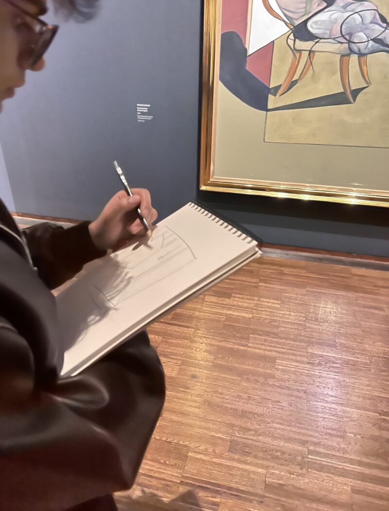 Schloss Krumbach International School student seated in an Albertina gallery with a sketchbook in front of exhibited artworks.
