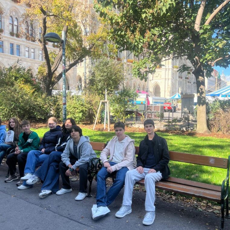 Schloss Krumbach International School students relaxing on park benches near Circus Roncalli and Vienna City Hall during their school trip.